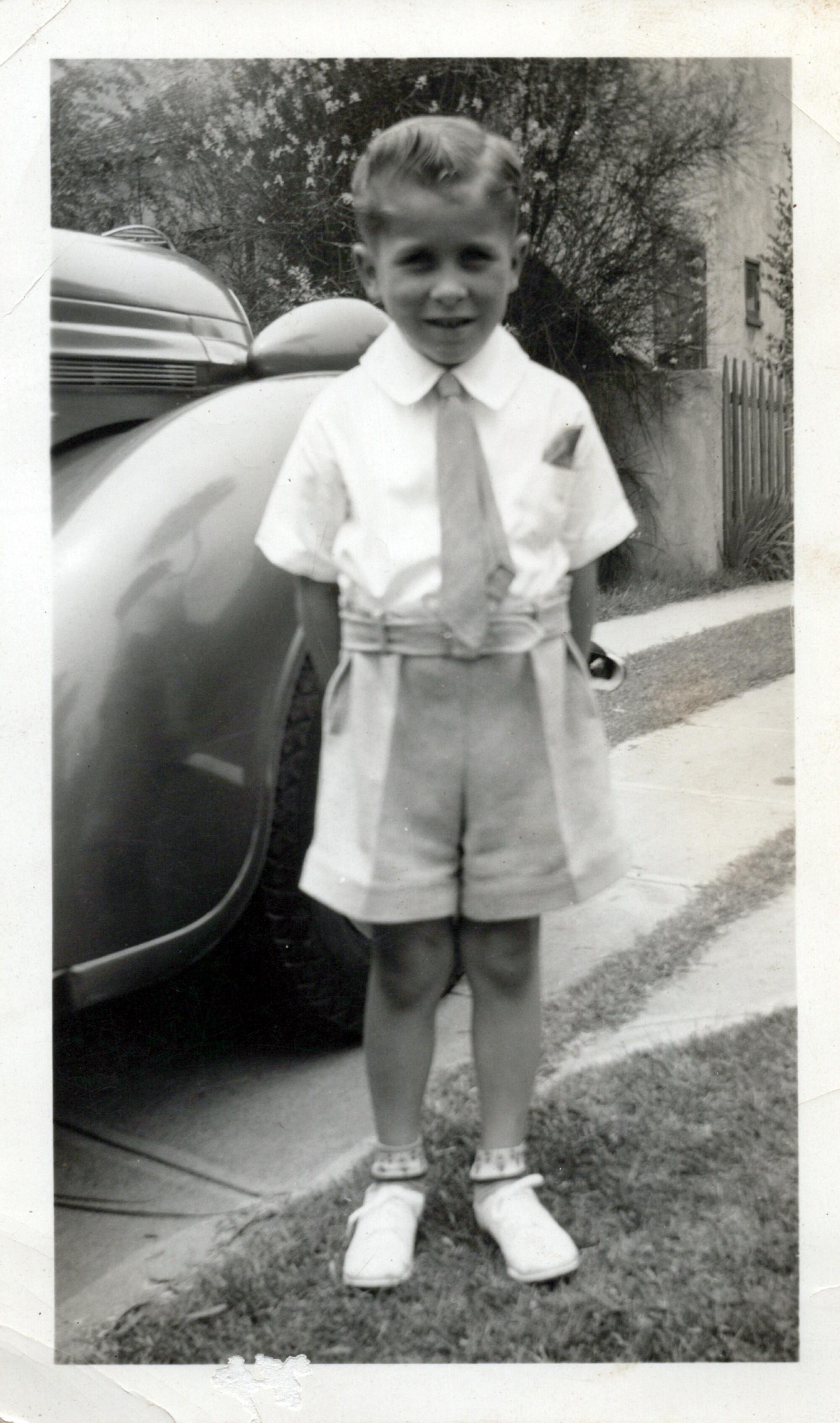 A young boy in a collared shirt with a tie and shorts.