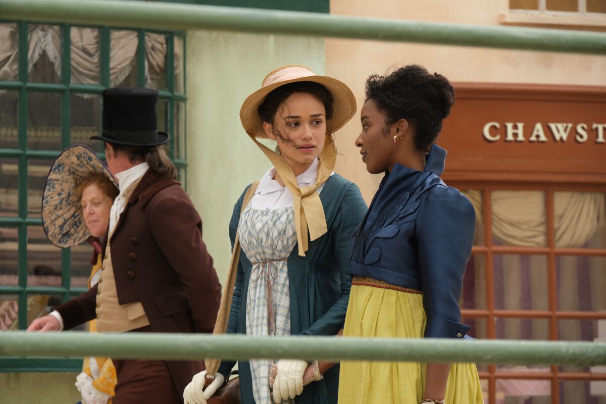 Two women walk in a seaside village in the early 1800s.