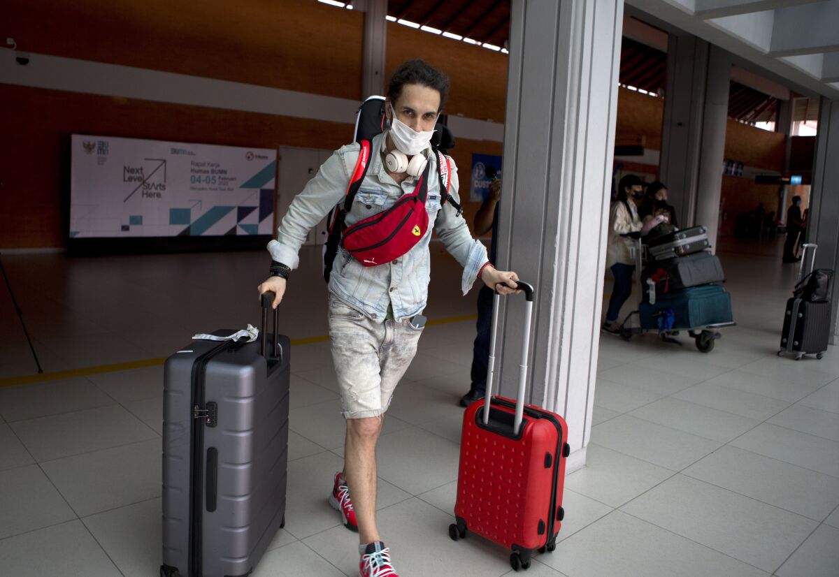 A Russian tourist carries his luggage upon his arrival at Bali's international airport, Indonesia on Friday, Feb. 4, 2022. Indonesia is opening the resort island of Bali to foreign travelers from all countries, as international flights resumed for the first time in two years — but mandatory quarantines remain in place for all visitors. (AP Photo/Firdia Lisnawati)