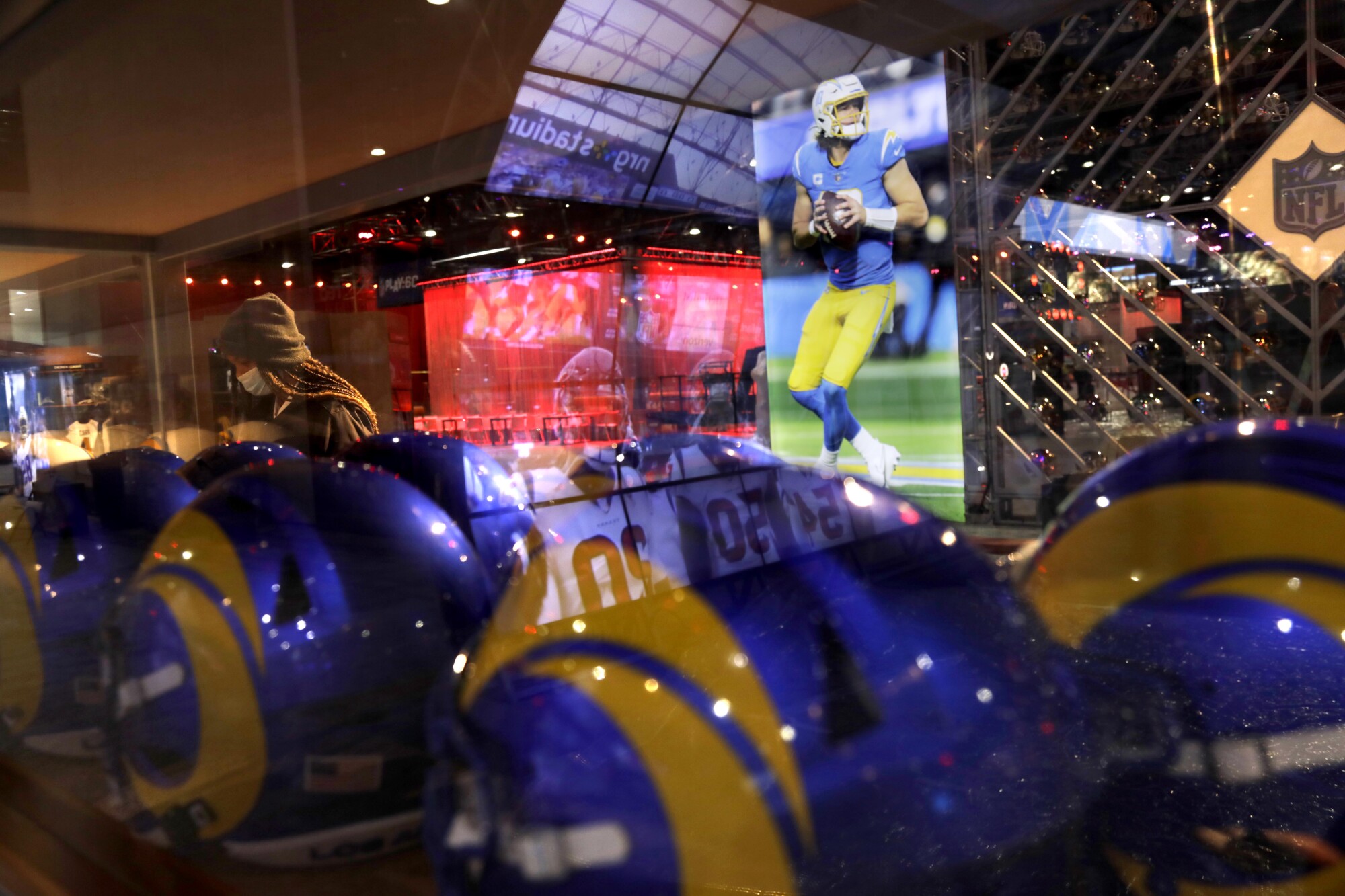 Rams helmets are seen through glass that reflects video images of football scenes