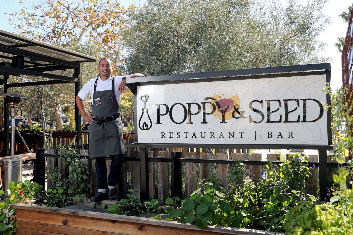 Chef Michael Reed stands beside the Poppy & Seed sign.
