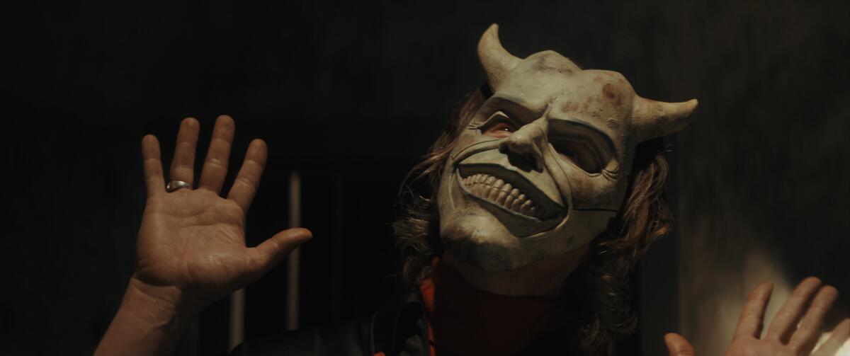 A person wearing a devil mask throwing his hands up in the air.