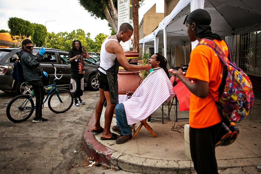 LEIMERT PARK, CA - JUNE 15: Jacket Rashad, a street barber, gives Karim Mejia Mawema, a food vendor, a haircut on Degnan Blvd. on Tuesday, June 15, 2021 in Leimert Park, CA. The Leimert Park community is excited for the reopening and is preparing for a huge Juneteenth block party. (Jason Armond / Los Angeles Times)