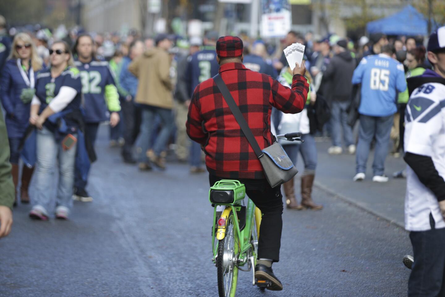 A scalper bicycles through a crowd with game tickets outside the stadium before an NFL football game between the Seattle Seahawks and the Los Angeles Chargers, Sunday, Nov. 4, 2018, in Seattle.