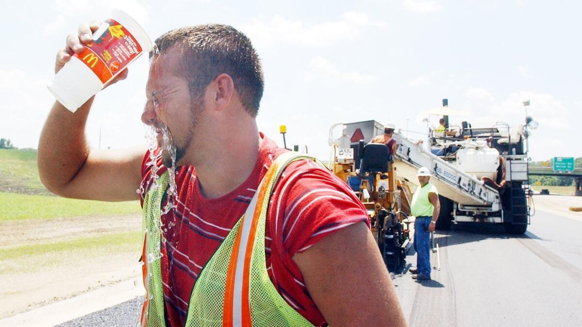 Adam Wilson of Griffin, Ind., cools off as road crews pave U.S. 41 during a 2006 heat wave. Across the country, lost labor productivity due to hotter temperatures could cost $155 billion per year by the end of the century.