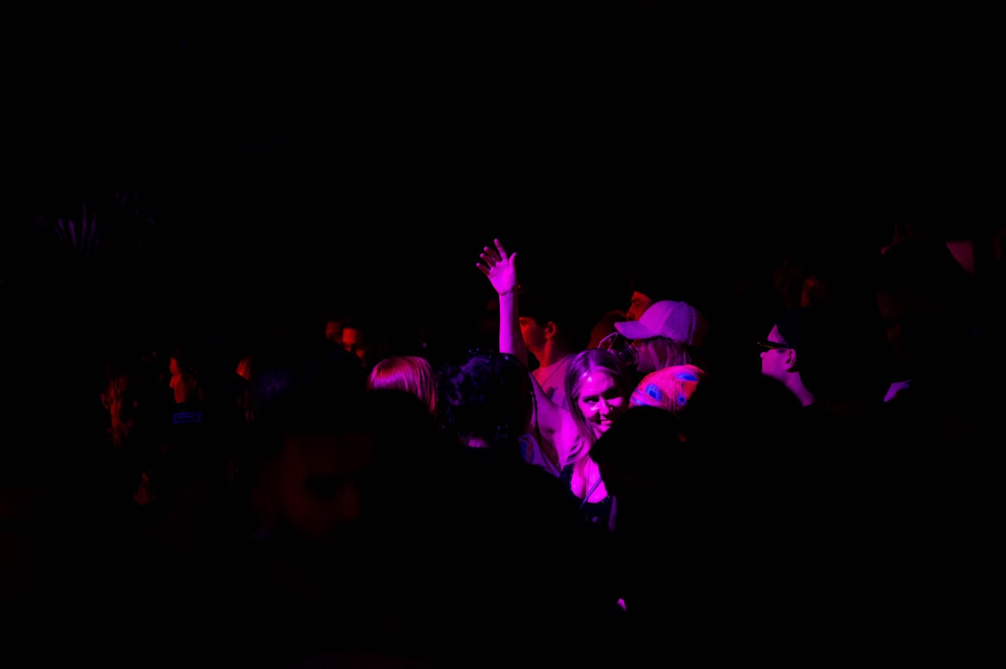 A woman is seen under a purple light dancing in a crowd.
