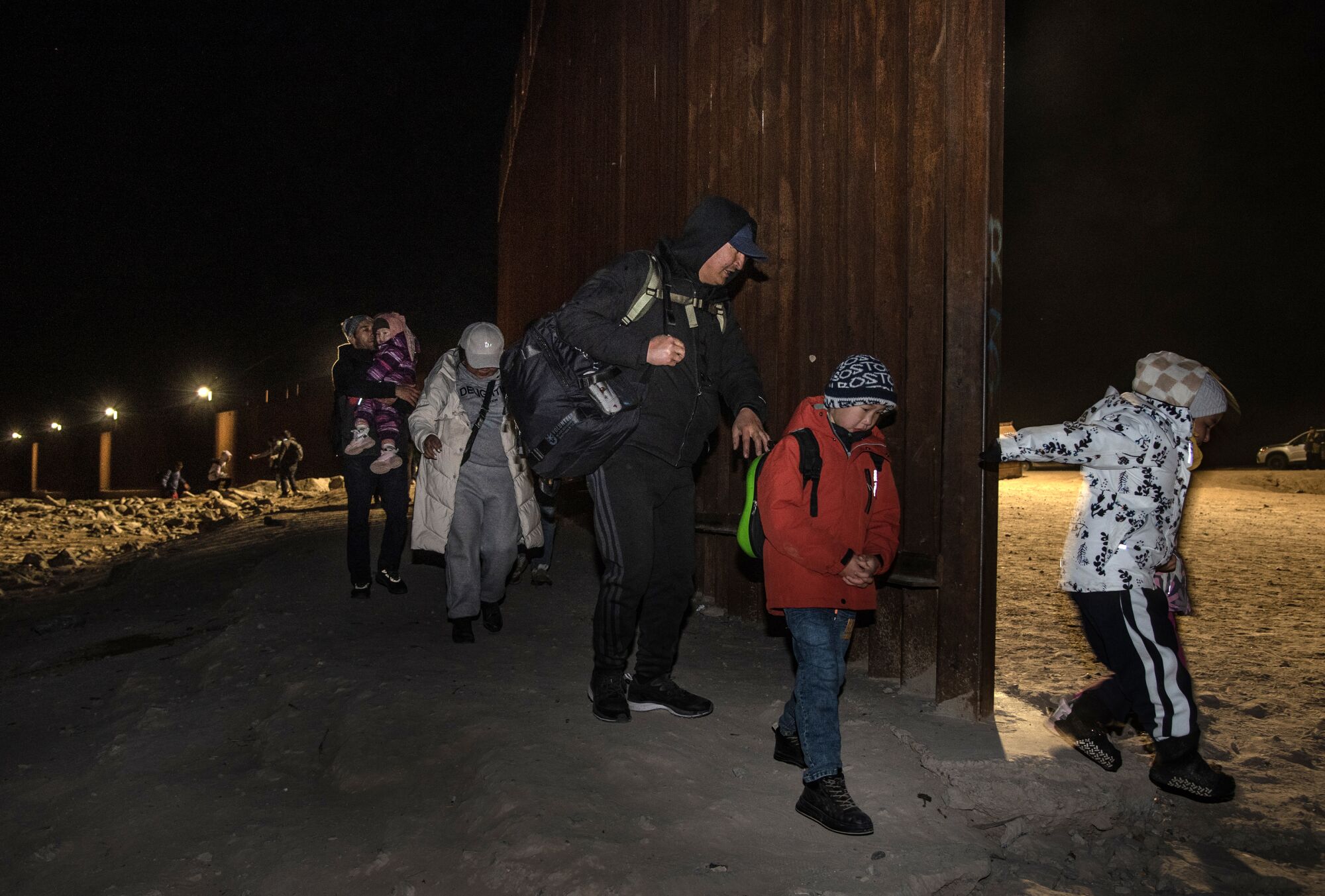 A family of adults and children walk around a gap in the U.S./Mexico border fence south of Yuma, Az.