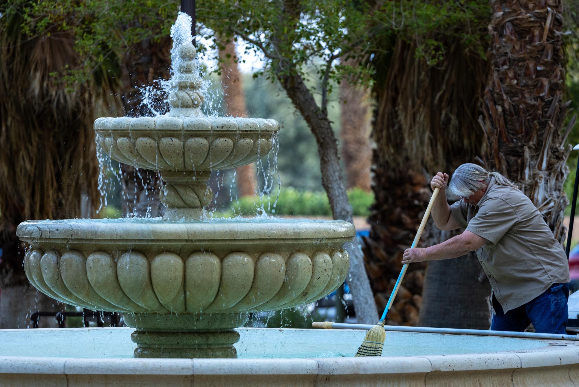 A worker uses a broom to clean a water fountain.