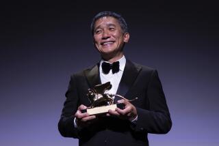 Tony Leung smiles while wearing a black tuxedo and holding a golden, lion-shaped trophy.
