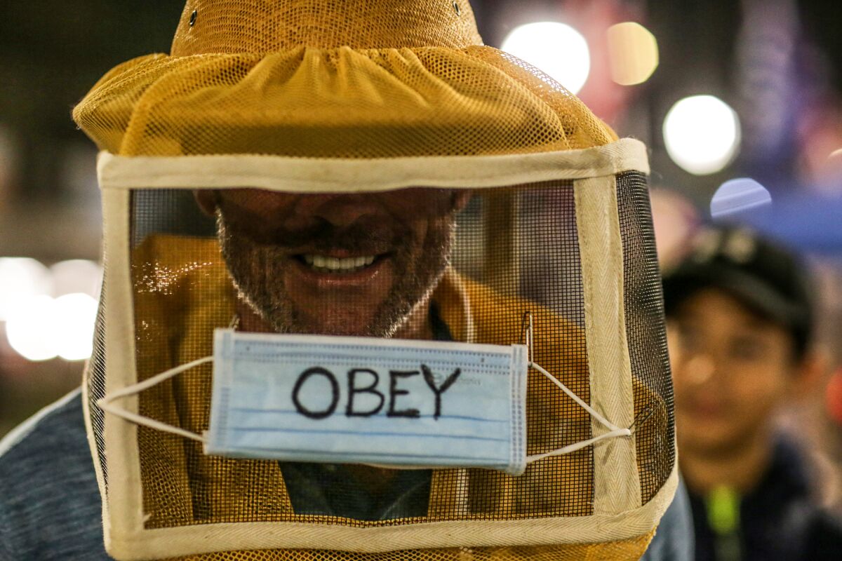 A Huntington Beach protestor against pandemic restrictions wears a see-through box labeled "OBEY" around his head.