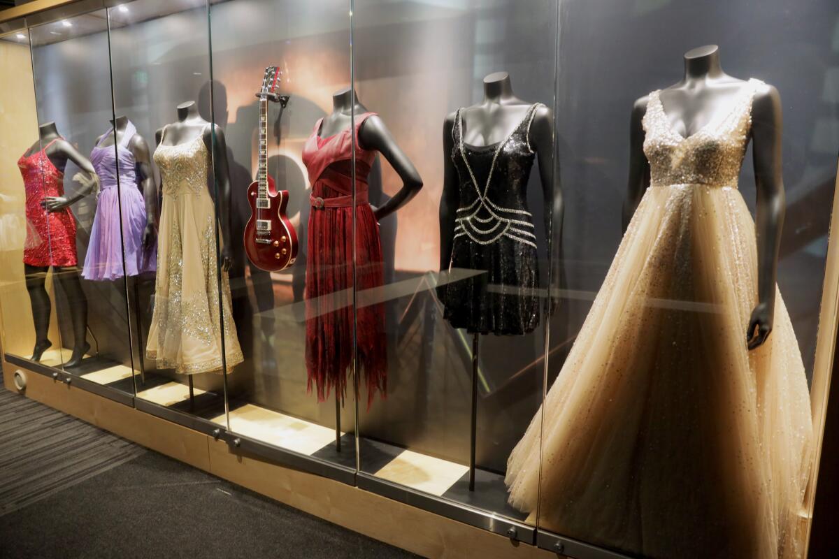 Dresses and a guitar behind a glass display.