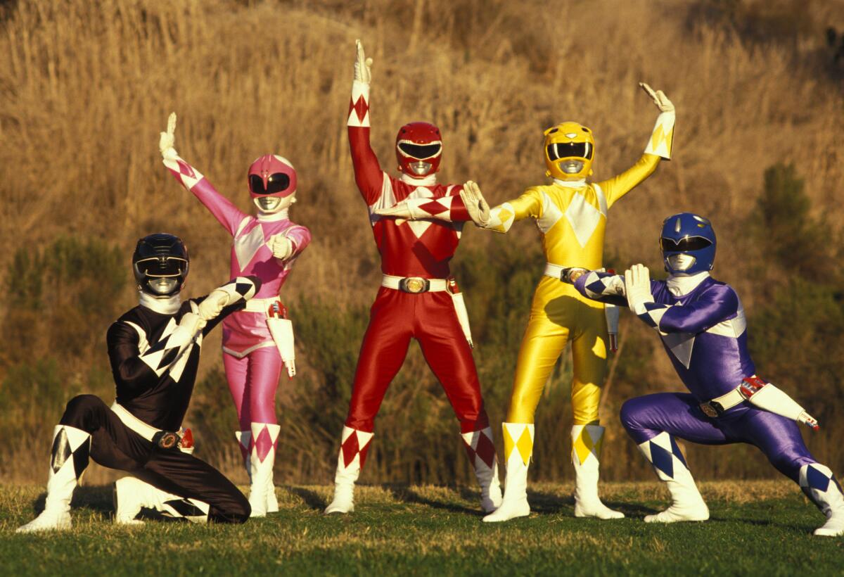 The black, pink, red, yellow and blue Power Rangers pose in a field.