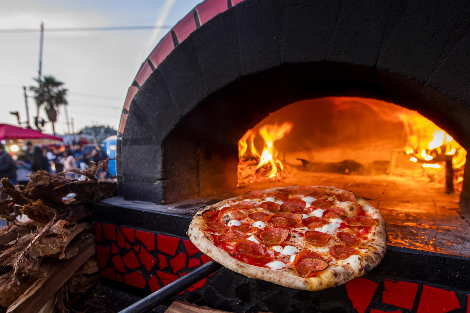 A pizza emerges from a wood-fired oven at an outdoor market.