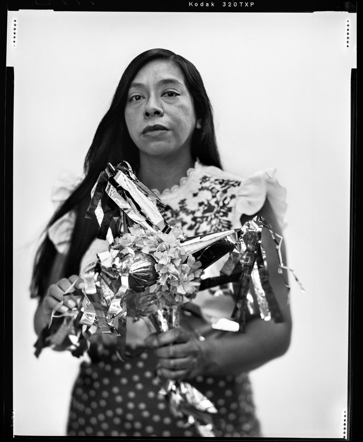 Black and white film photo of a Mexican woman, Michelle Reyes, holding a starburst-shaped piñata