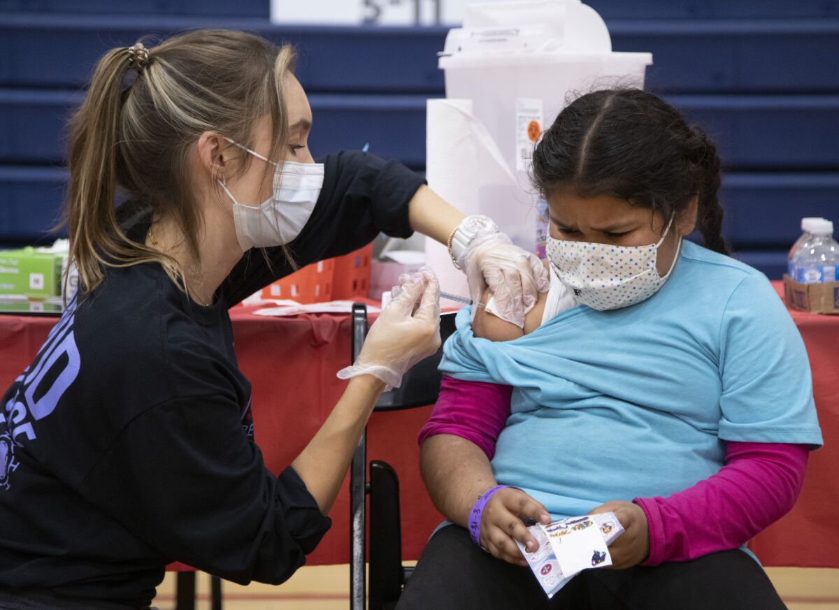 A nurse gives a COVID-19 vaccine to a nervous 7-year-old.
