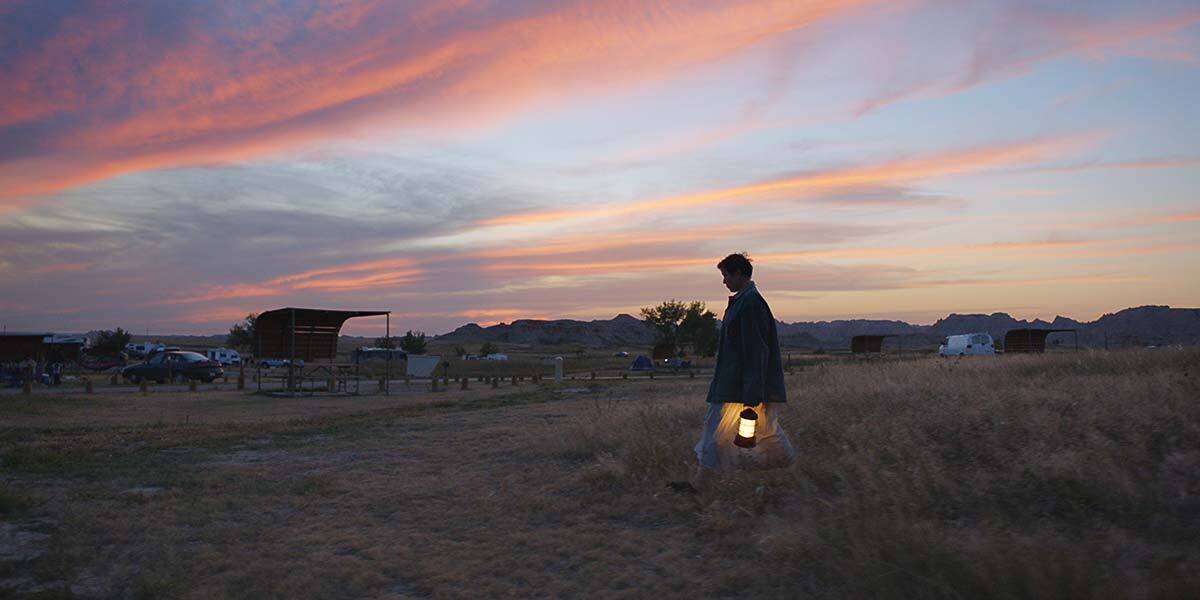 Frances McDormand holds a lit lantern while walking through a field