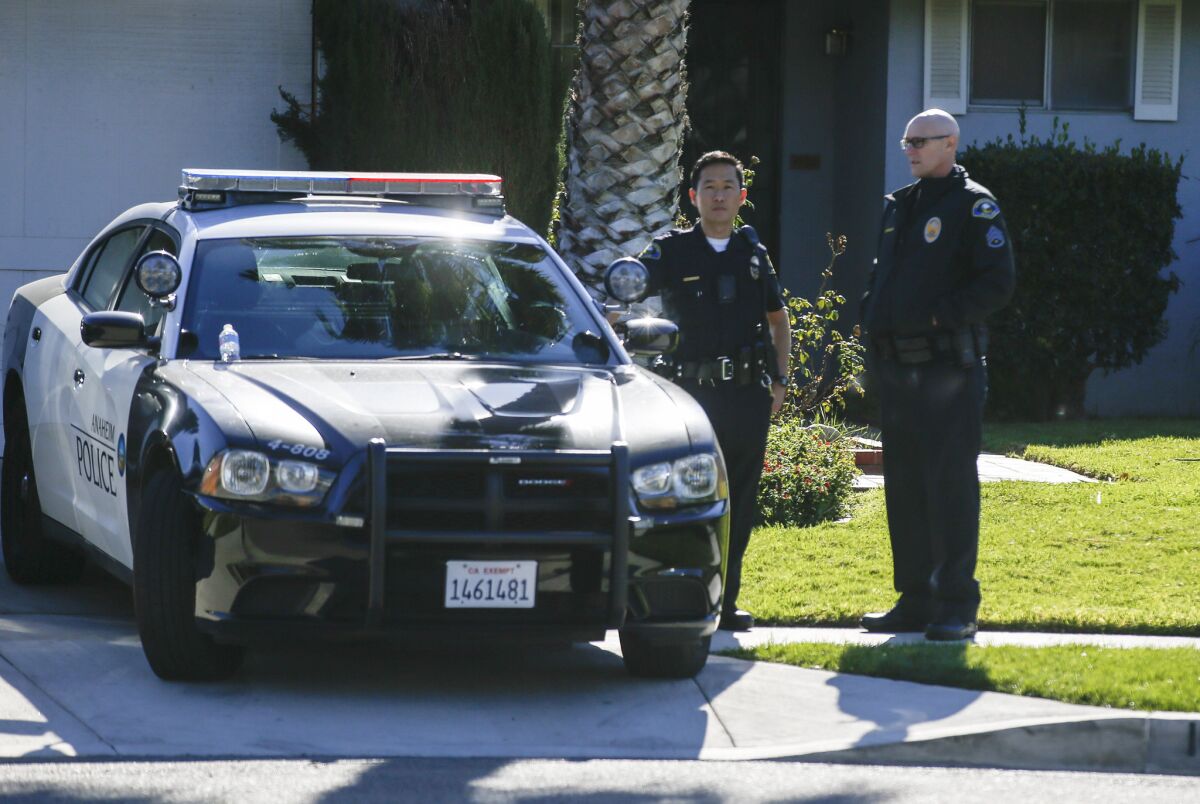 Several Anaheim police officers keep watch over the neighborhood while crime scene investigators collect evidence left behind by protesters at the home of an LAPD officer in Anaheim.
