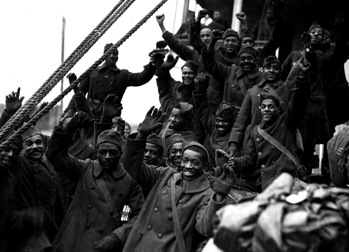 On a boat deck, Black servicemen wave and smile.