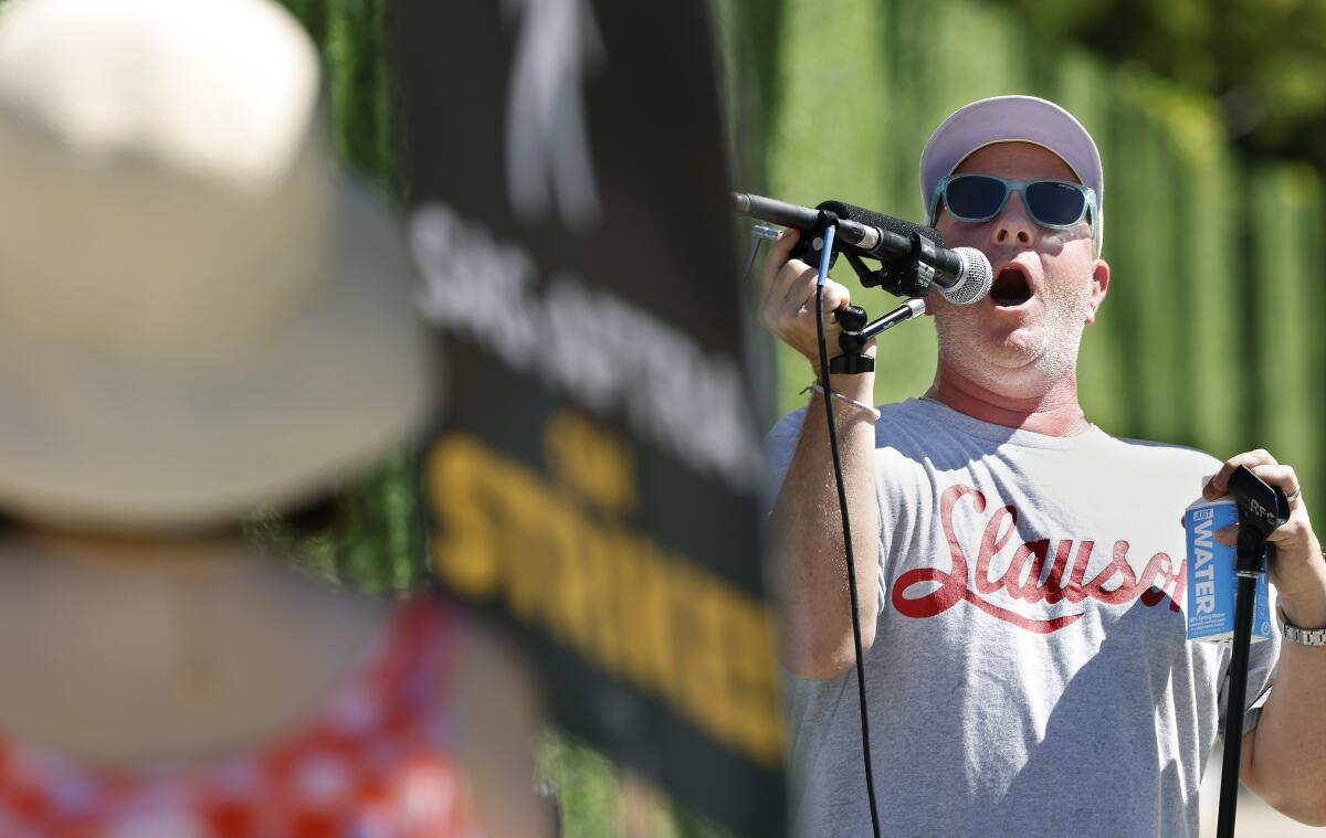 A man in sunglasses and a cap speaks into a microphone at a rally.