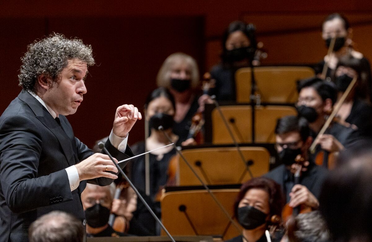 A man with curly hair wearing a suit and holding a conductor's baton