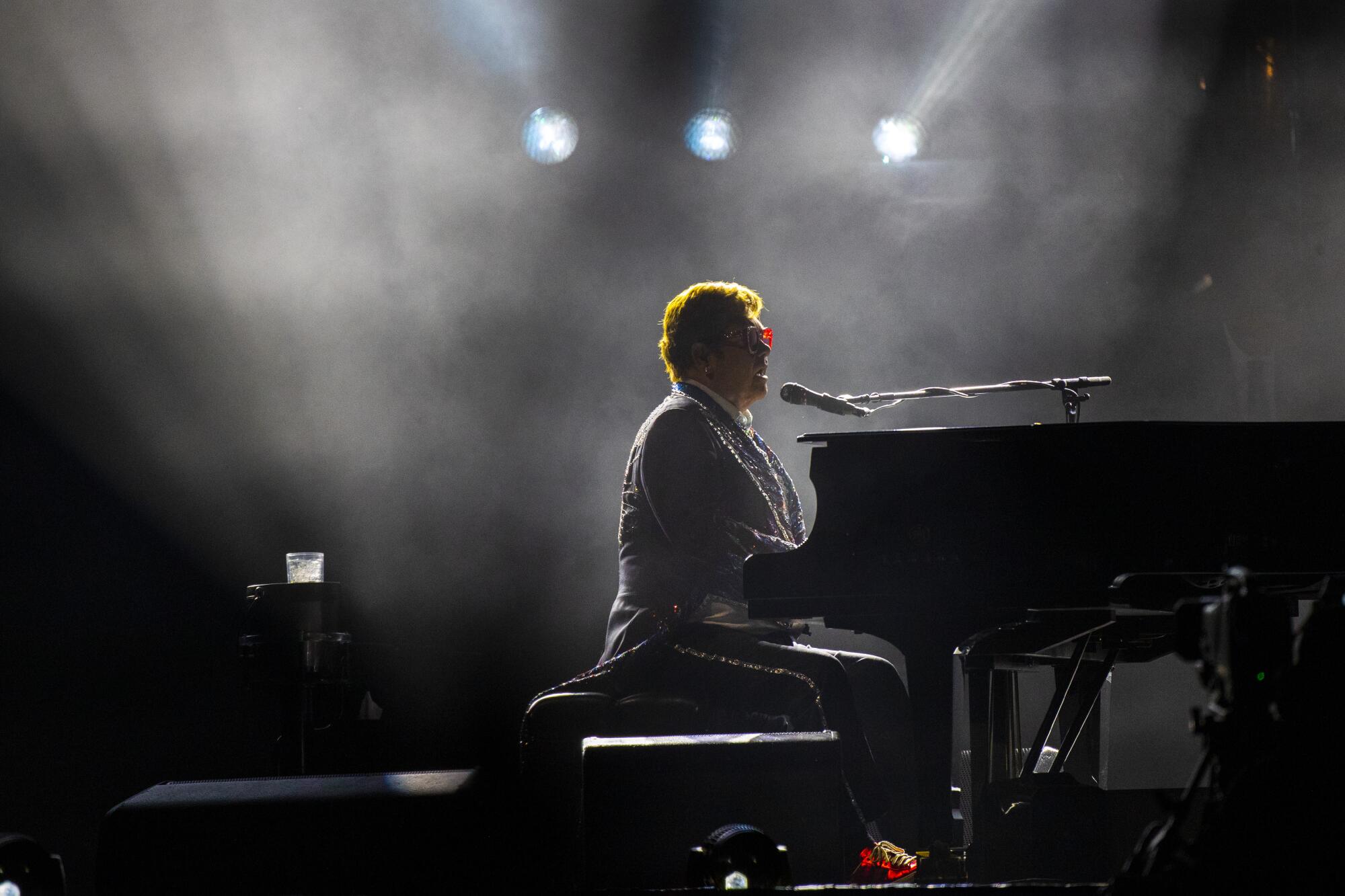 A foggy silhouette of a man playing piano and singing into a microphone on a stage