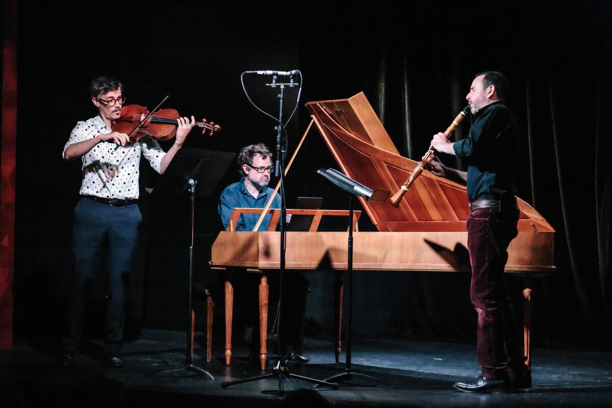 A standing violinist and clarinet player next to a seated fpiano player on a darkened stage