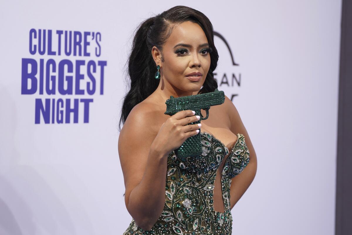 Angela Simmons showing off a bedazzled green purse shaped like a handgun while wearing a strapless green gown