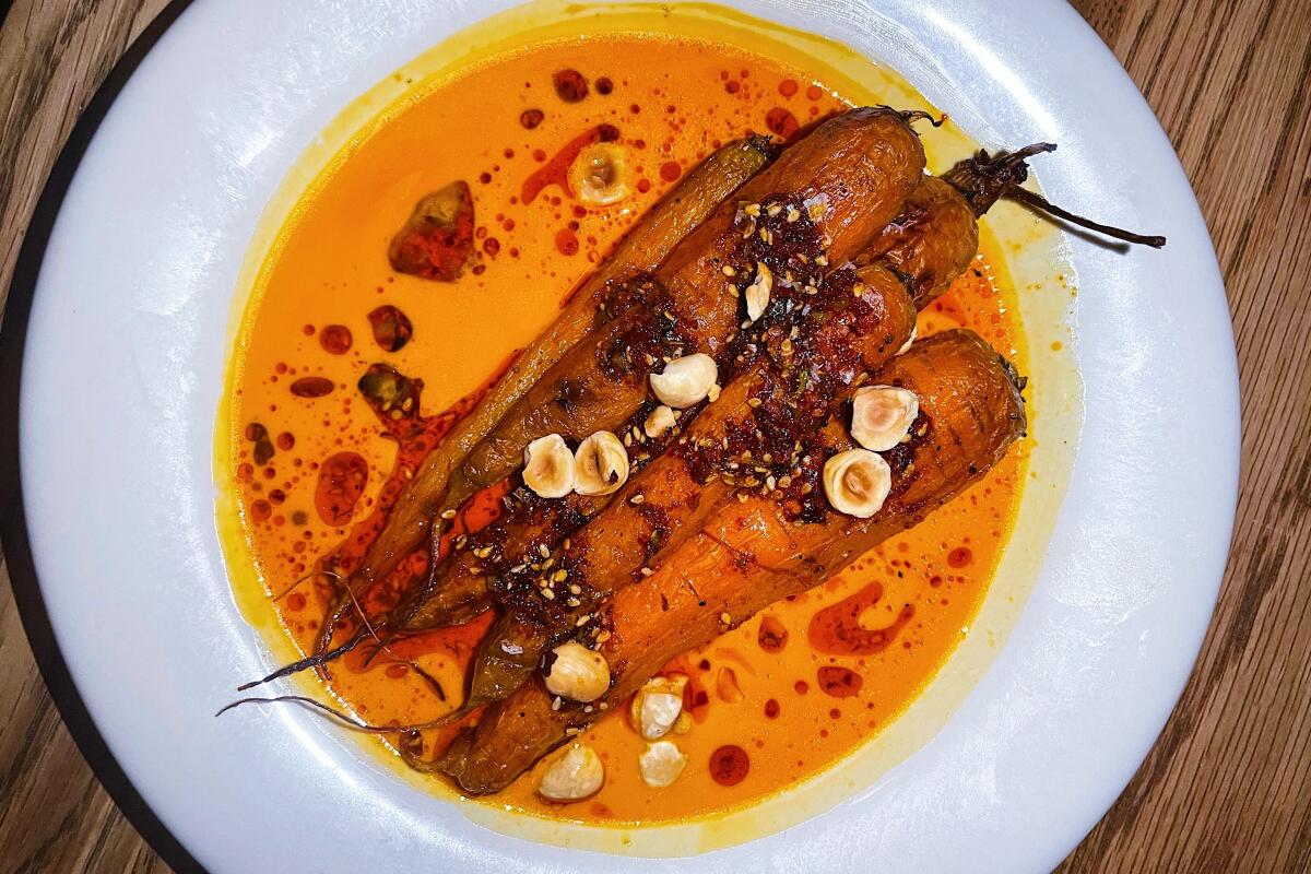 An overhead photo of whole roasted carrots in a pool of bright orange carrot butter sauce at Stir Crazy wine bar on Melrose