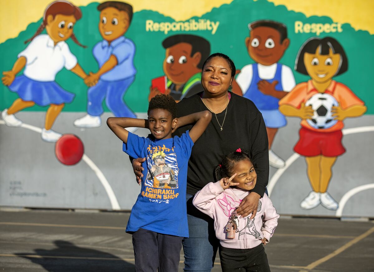 A woman and two children stand in front of a mural showing children at play and the words "responsibility" and "respect."
