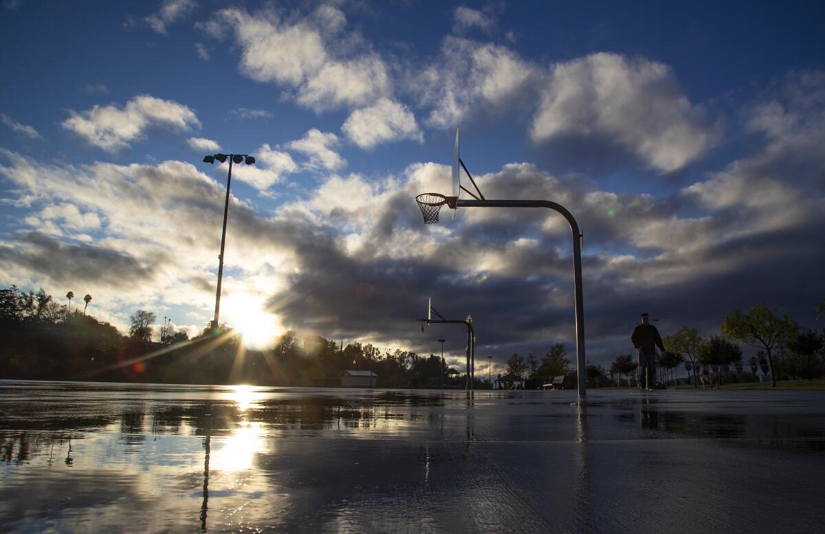 The sun shines behind clouds over a wet outdoor basketball court.