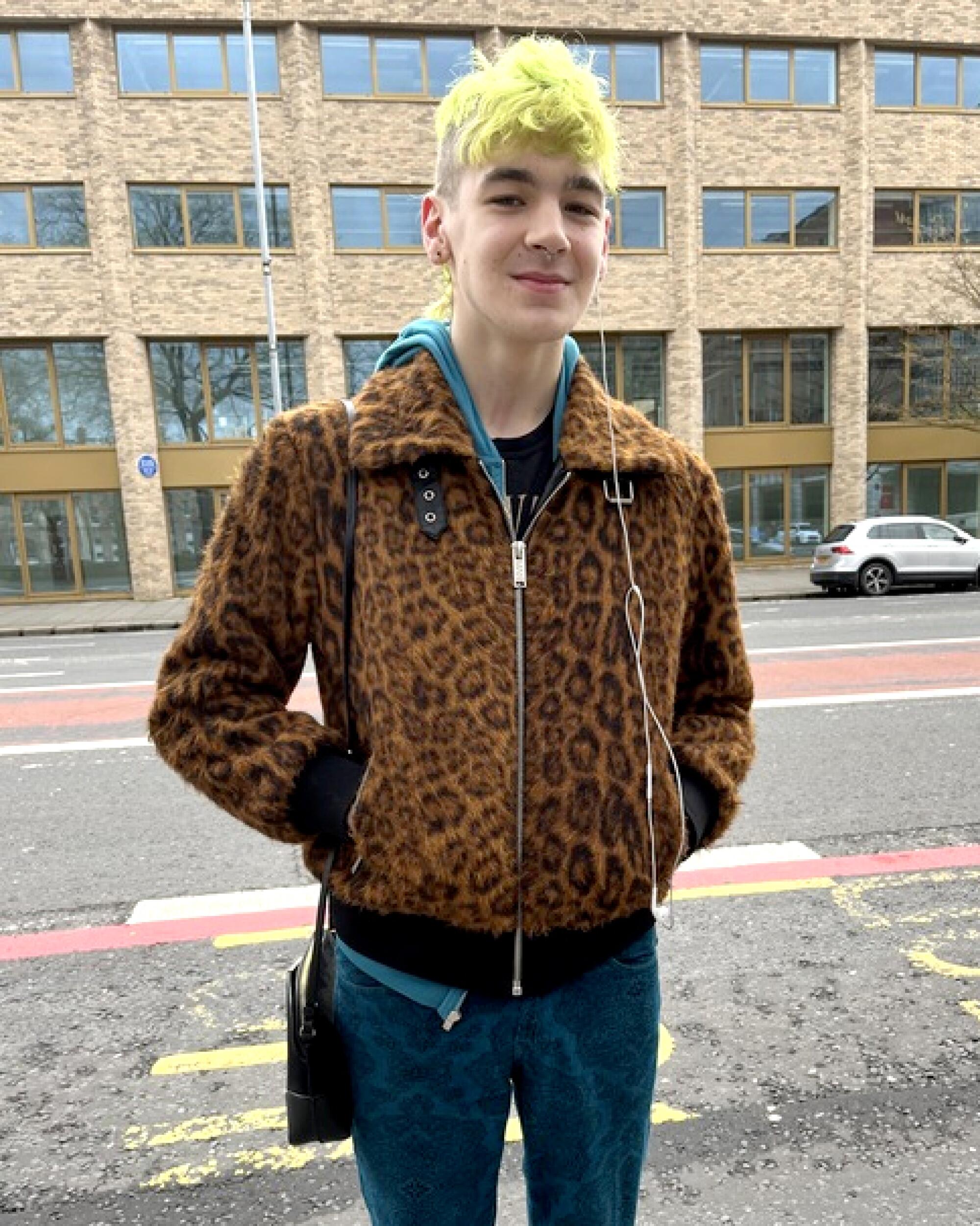 Lars Jackson wears a leopard-print jacket and has neon-green hair. Lars is standing on a street.