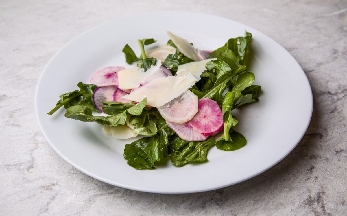 A plate of greens with radishes on top 