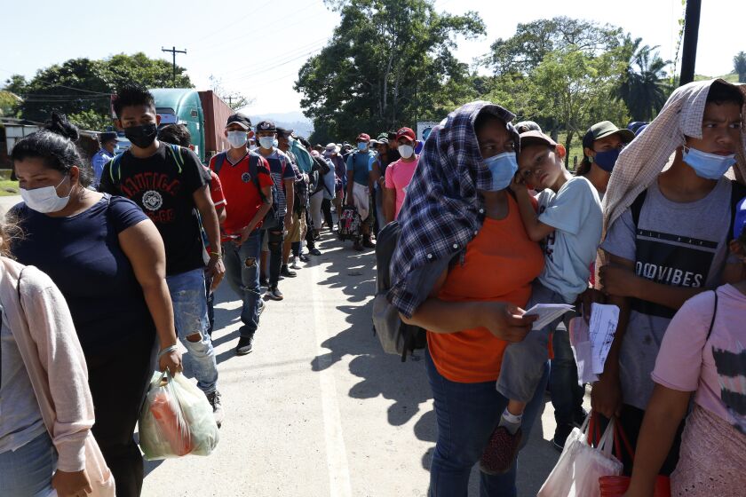 Migrantes que forman parte de una caravana que aspira con llegar a Estados Unidos esperan en una línea para que agentes de la policía revisen su documentación en Corinto, Honduras, el sábado 15 de enero de 2022. (AP Foto/Delmer Martínez)