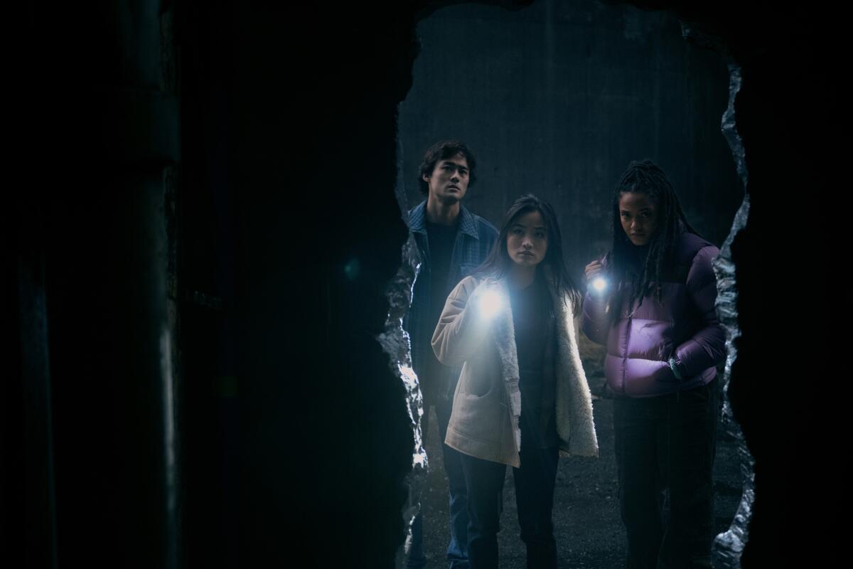 Ren Watabe, Anna Sawai and Kiersey Clemons peer into a hole in a wall with flashlights