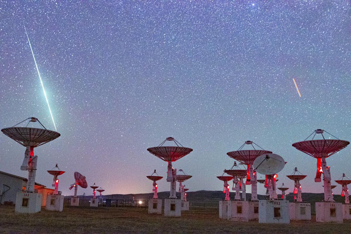 Meteors create streaks of light across the sky above equipment at an observatory.