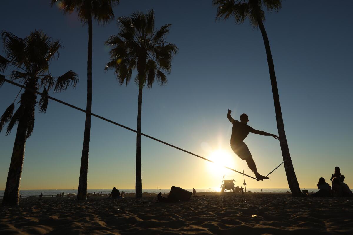 A man tries to maintain his balance on the slack line in Venice Beach as the sun sets.