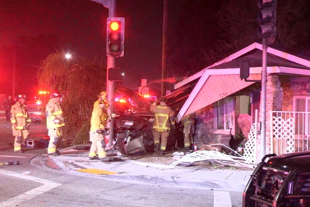 First responders examine a wrecked gray Nissan Maxima that crashed in a house at an intersection