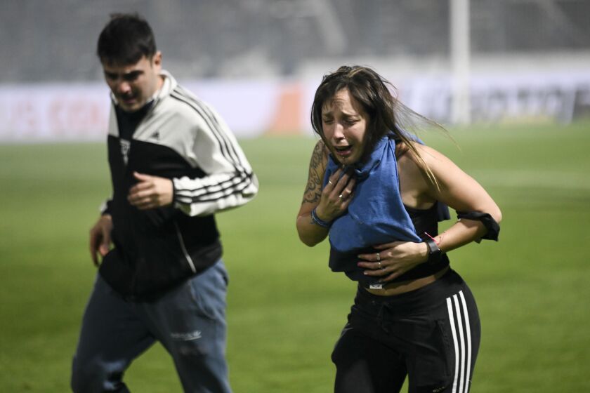 Fans of Gimnasia de La Plata choke on tear gas during a local tournament match between Gimnasia de La Plata and Boca Juniors in La Plata, Argentina, Thursday, Oct. 6, 2022. The match was suspended after tear gas thrown by the police outside the stadium wafted inside affecting the players as well as fans who fled to the field to avoid its effects. (AP Photo/Gustavo Garello)