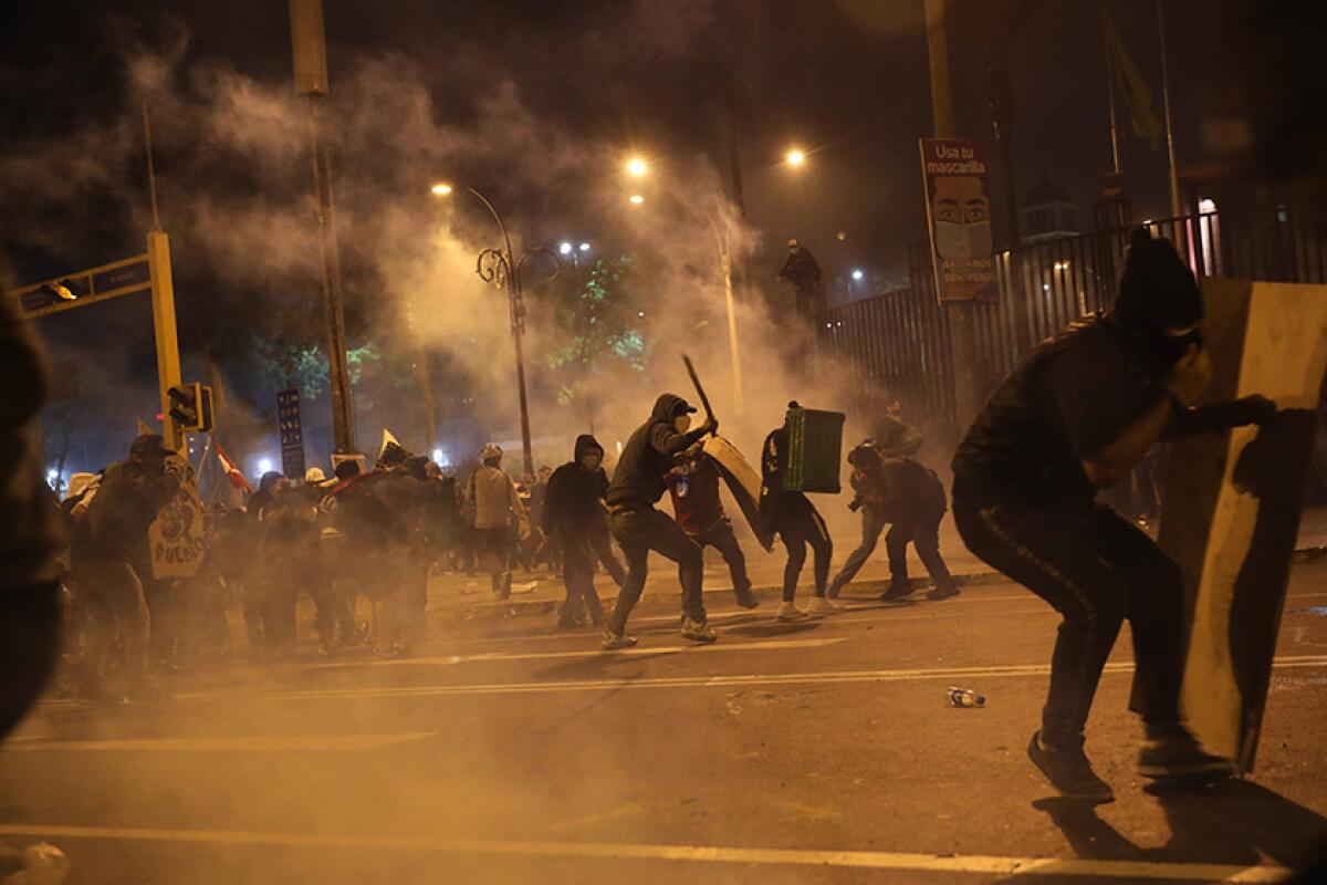 Protesters on the street hold up makeshift shields amid tear gas.