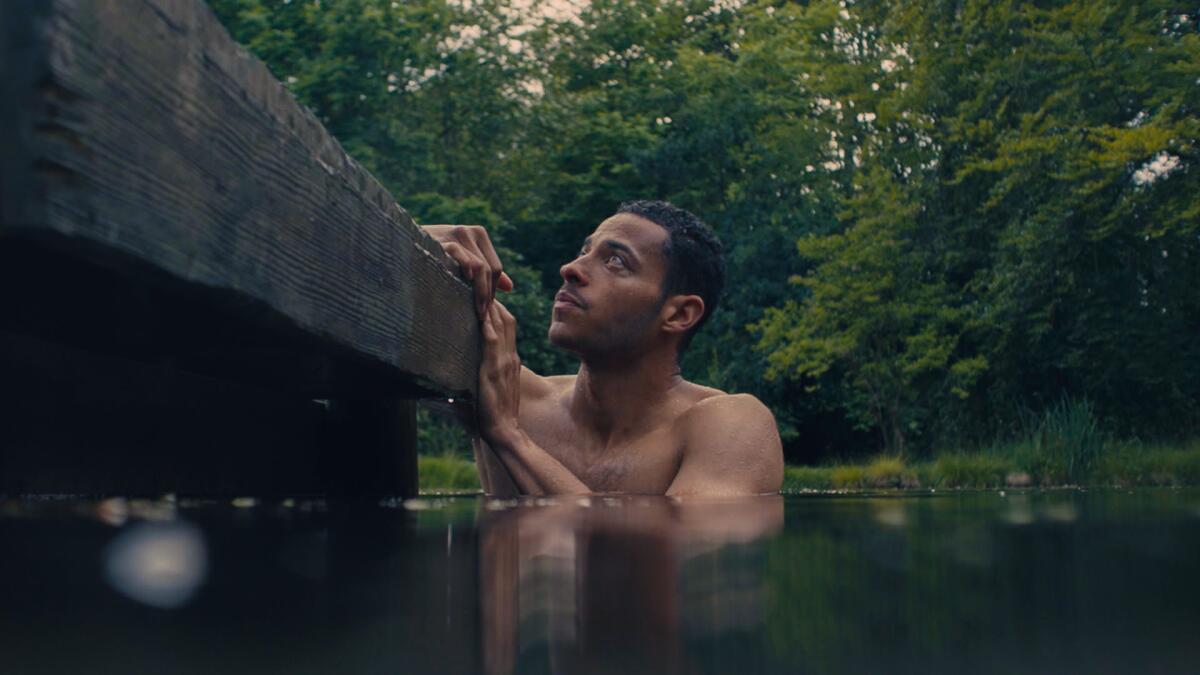 A man swims in a lake by a wooden pier.