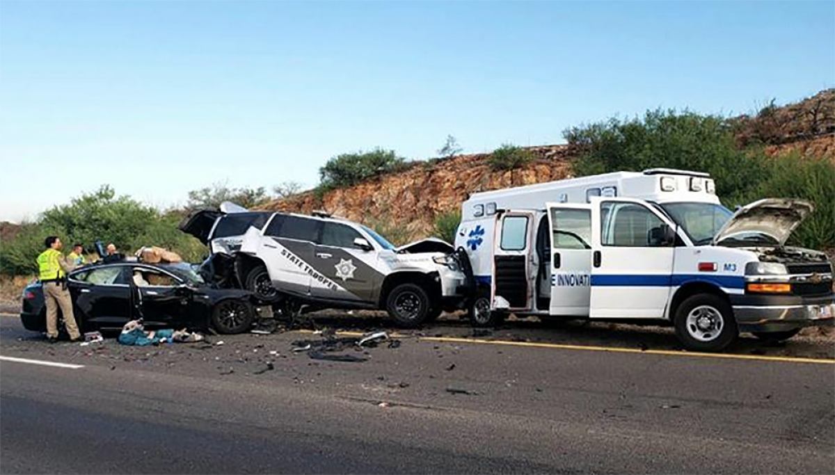 A crash scene involving a Tesla, a police vehicle and an ambulance.