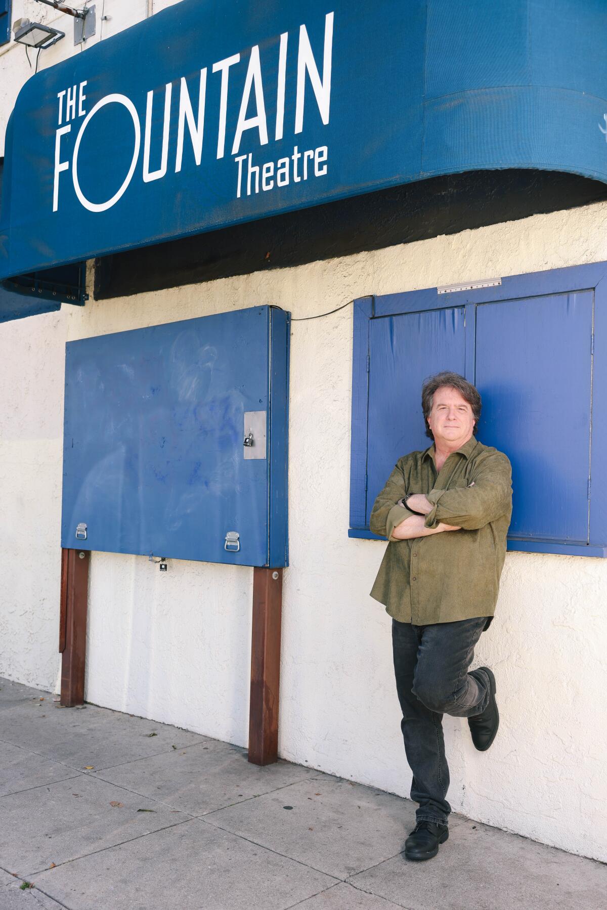Stephen Sachs, in an olive shirt, stands underneath the blue marquee of the Fountain Theatre.