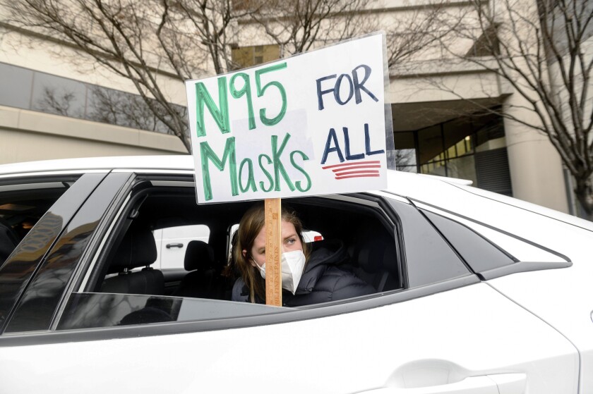 A teacher holds a sign outside her car window during a protest  for stronger COVID-19 safety protocols.