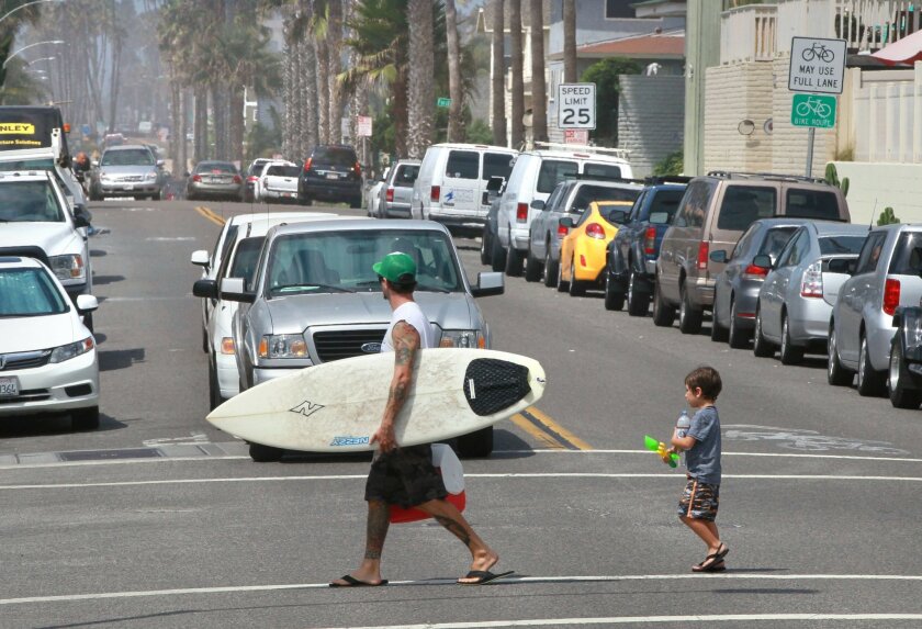  A man and child cross South Pacific Street in Oceanside, where many vacation rentals are located. 