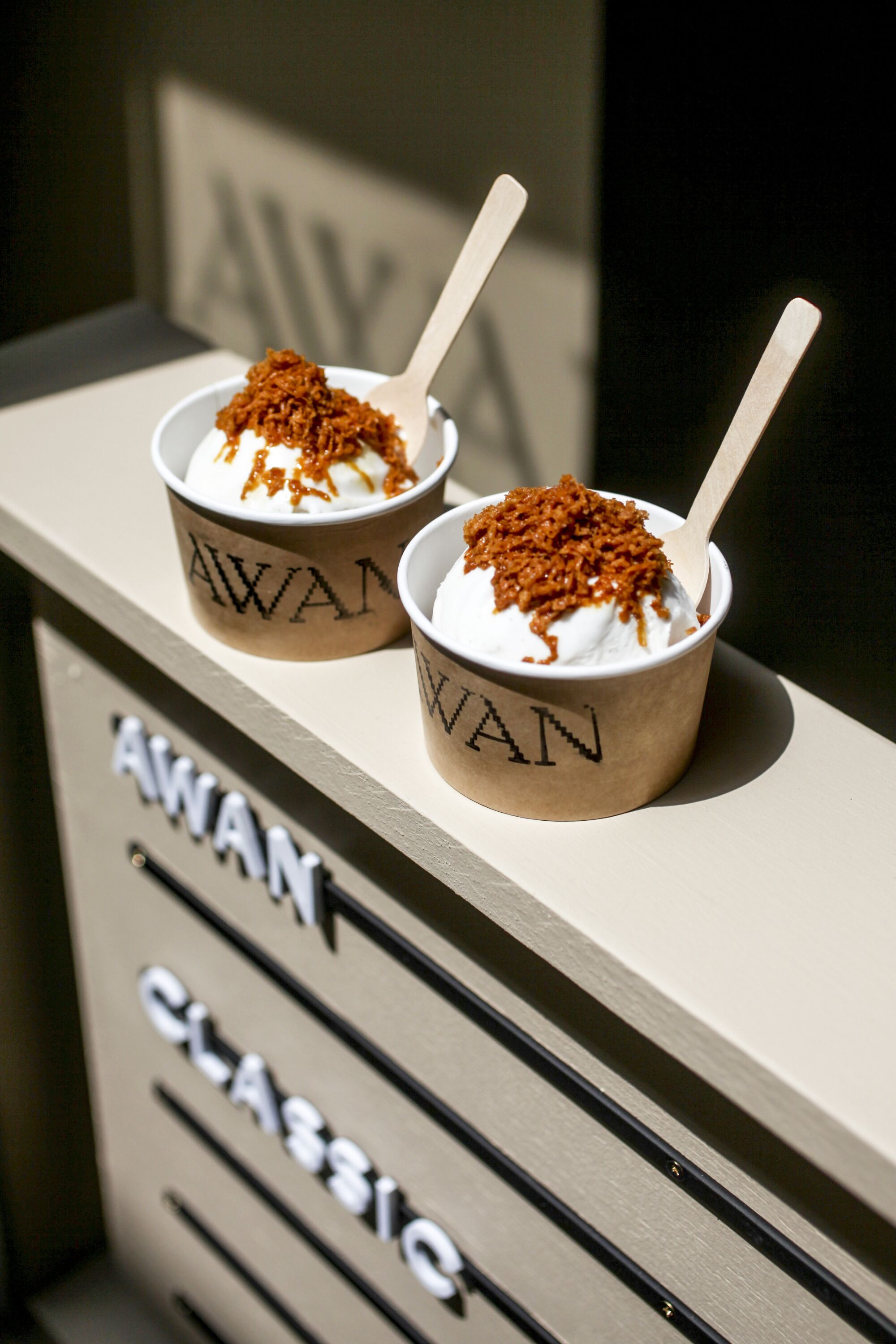 Two cups of vanilla gelato topped with shaved sugar at the ledge of an ordering window at Awan.