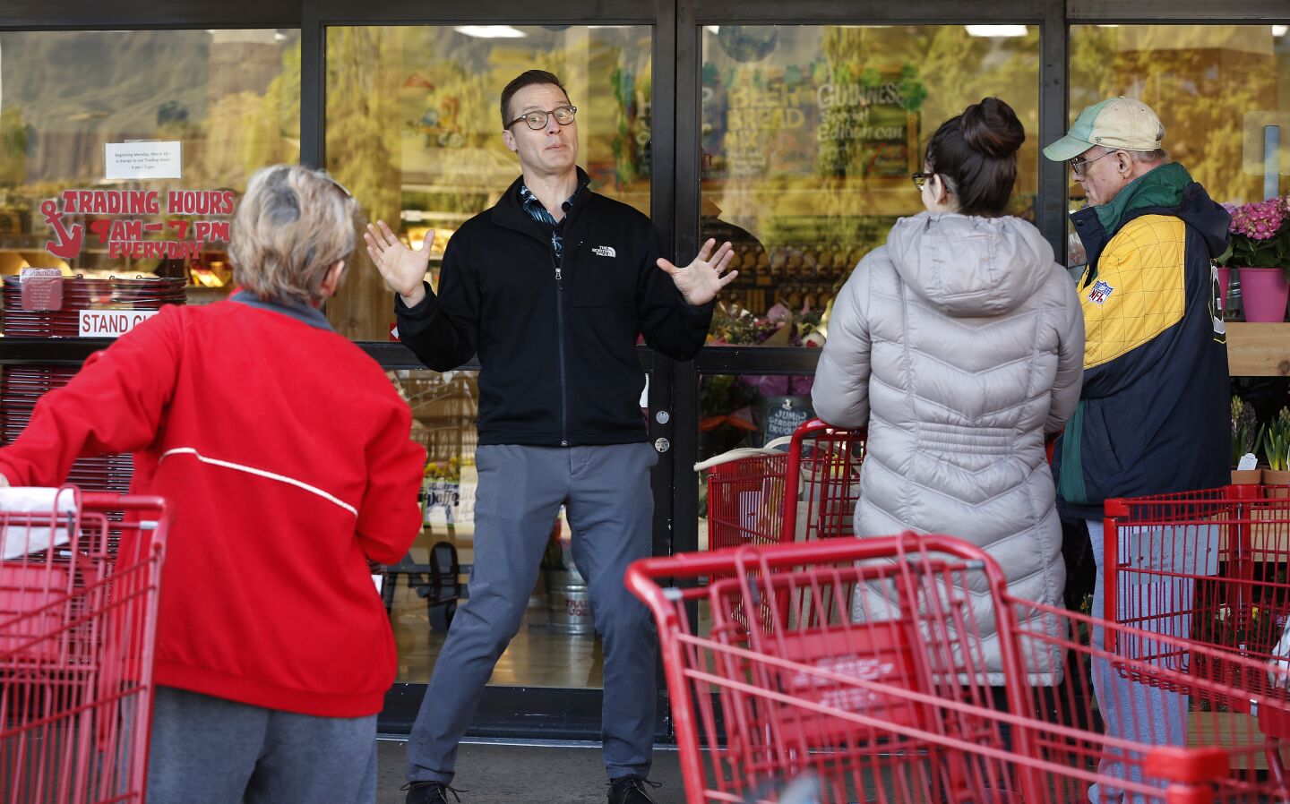 An employee of the Trader Joe's store in Monrovia tells customers waiting in line that it would open doors to everyone at 9 a.m., not just seniors, who arrived believing doors would open earlier to older residents, as some of the people were told by employees and it was reported. Some grocery outlets were offering special morning hours of shopping to accommodate older residents.