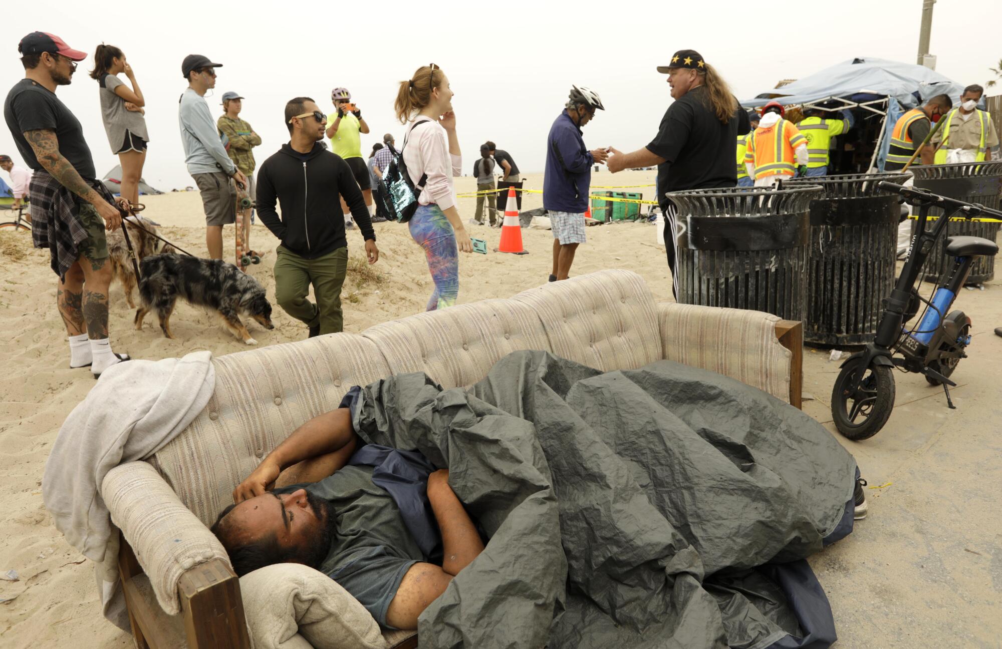 July 30: A homeless man sleeps on a couch as sanitation crews clear a homeless encampment on the beach