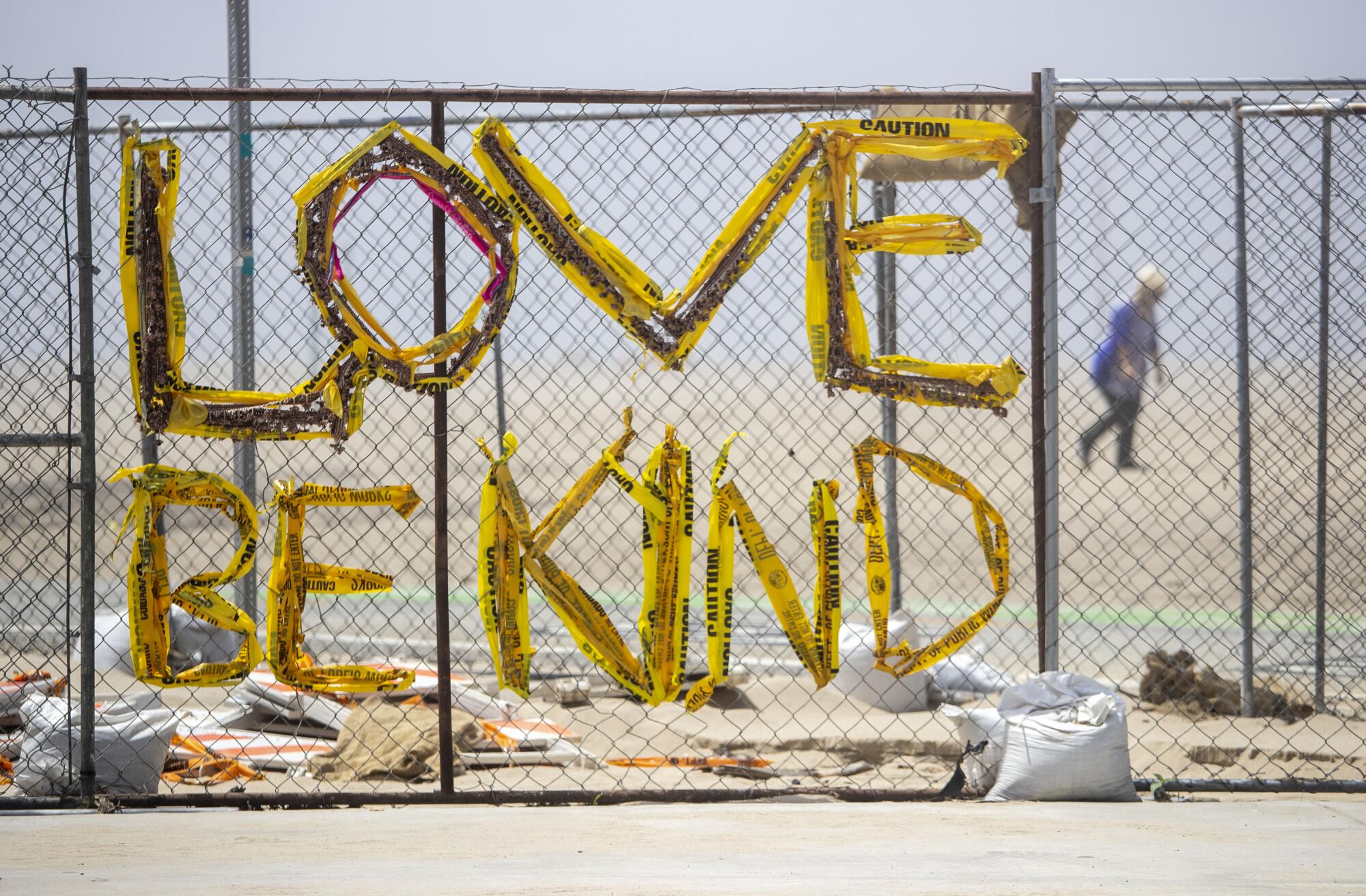 A message of positivity is woven with yellow police tape into a fence at a closed Venice beach.