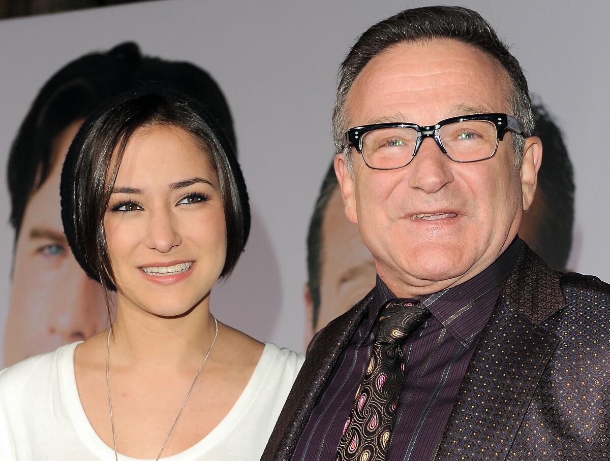 A young woman with short black hair in a white shirt smiling next to Robin Williams in glasses and a dark suit