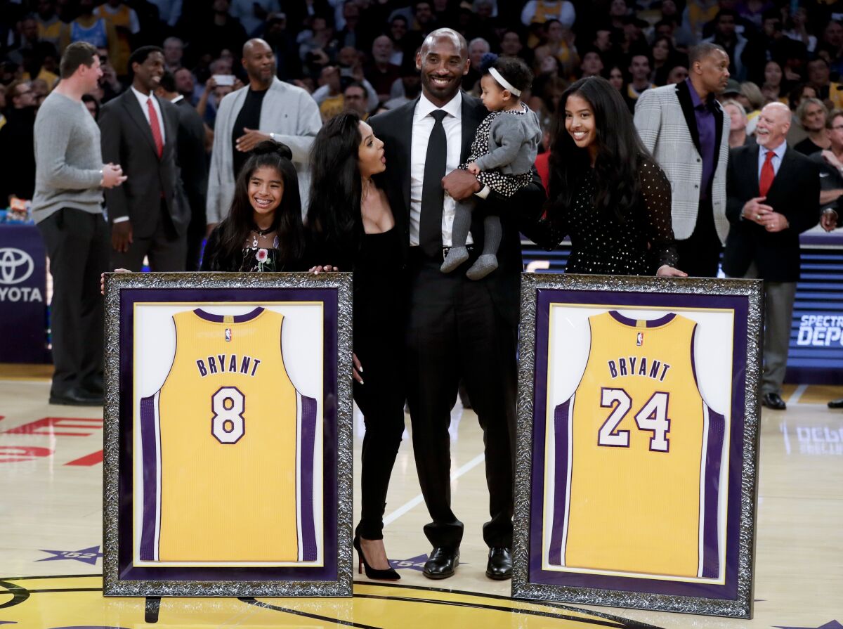 Kobe Bryant flanked by two girls, one woman and holding a baby on a basketball court.